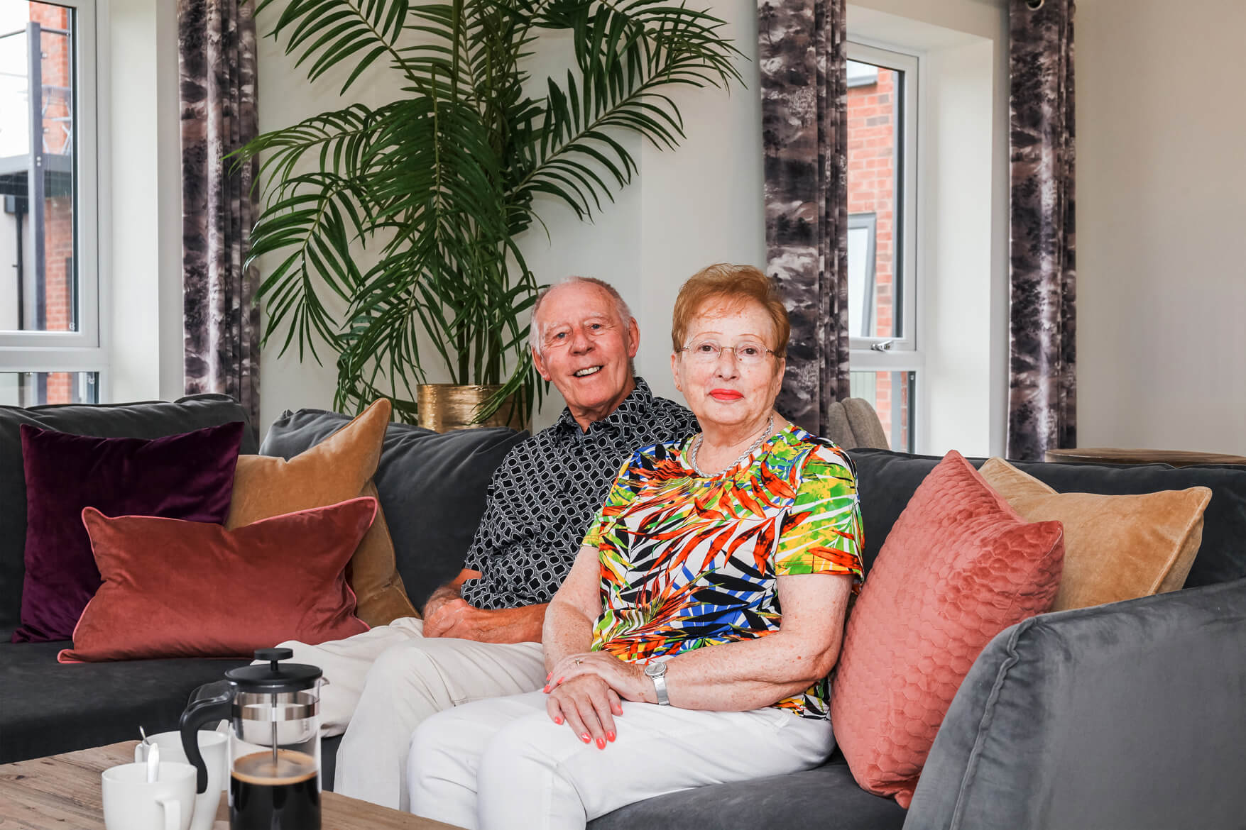 Homeowners enjoying their Broadleaf House apartment sat on their sofa smiling with fresh coffee